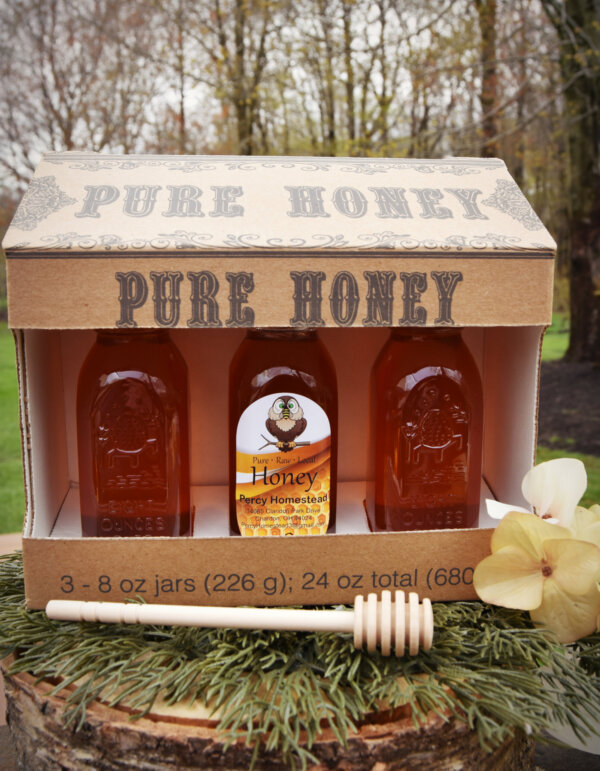 8 oz gift box with 3 muth bottles on pine needle base and treed background, white flower by the box and a 6" dipper stick in front of the box.