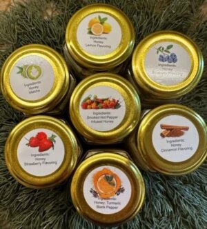 This is a picture of 7 creamed honey products of the lid and flavor stickers, Match, Lemon, Blueberry, Smoked Hot Pepper Cinnamon, Strawberry and Turmeric with Black pepper