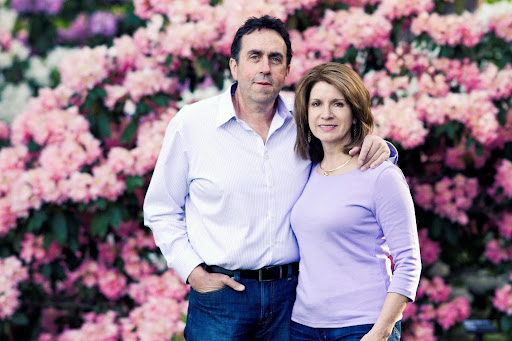 John and Cindy Gaul - Owners of Percy Homestead A man and a woman standing in front of pink hydrangeas.